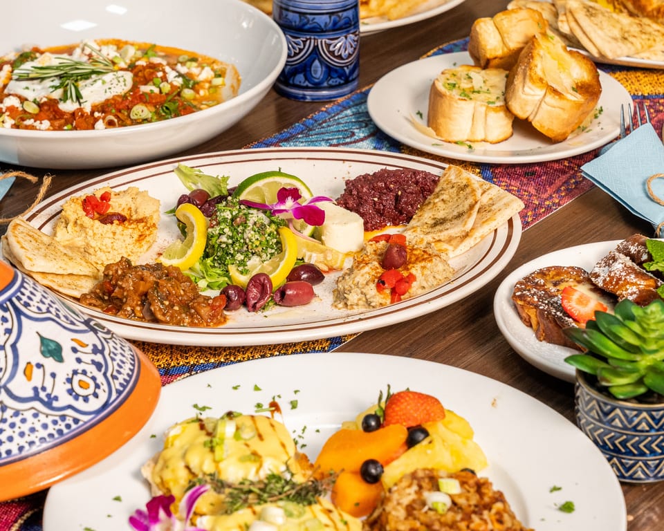 A table laden with various Moroccan dishes, including shakshuka, a mezze platter, and French toast.