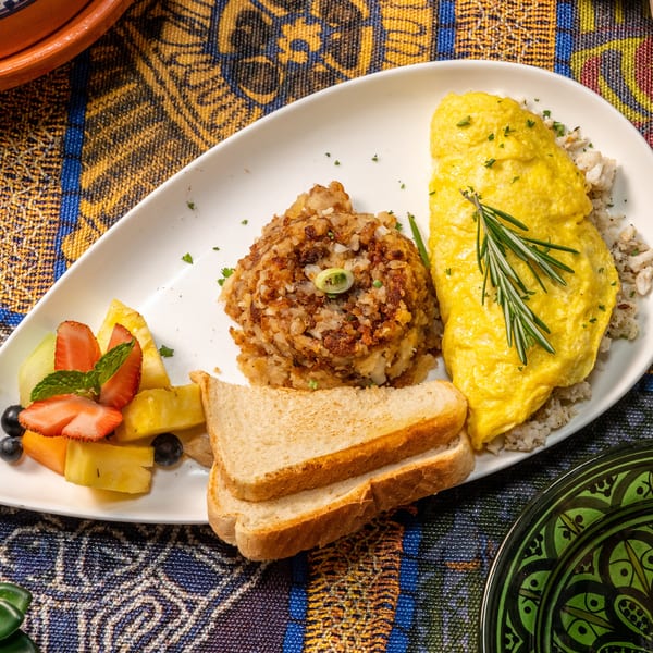 A breakfast plate with an omelet, hash browns, toast, and fruit salad on a colorful patterned tablecloth.
