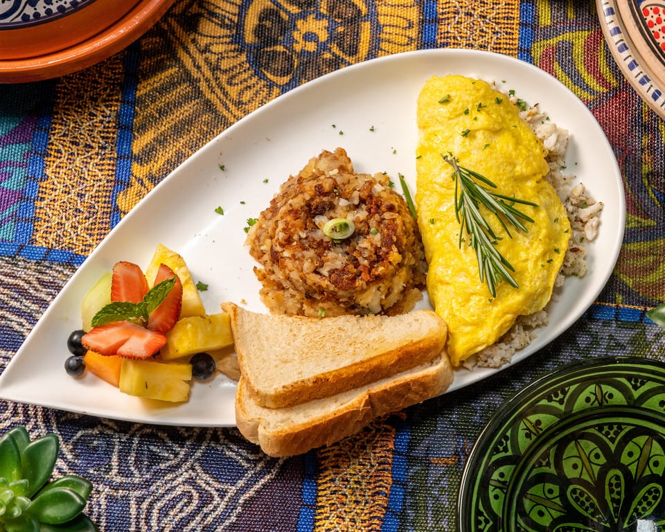 A breakfast plate with an omelet, hash browns, toast, and fruit salad on a colorful patterned tablecloth.