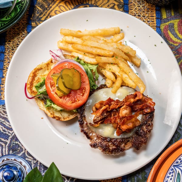 Overhead view of a bacon cheeseburger with fries, tomato, onion, and pickles on a white plate.