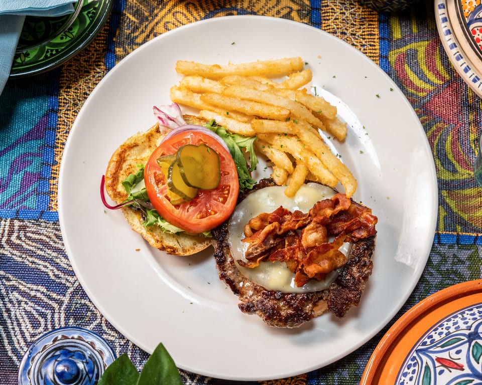 Overhead view of a bacon cheeseburger with fries, tomato, onion, and pickles on a white plate.