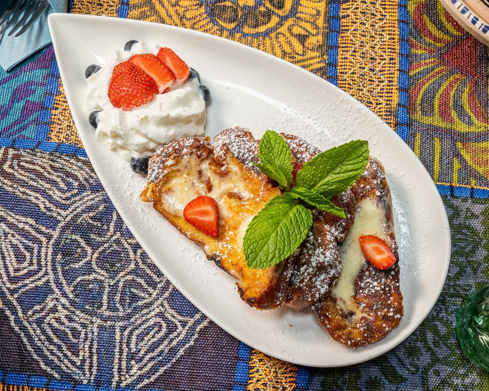 Golden French toast with powdered sugar, cream, strawberries, blueberries, and mint on a white plate.