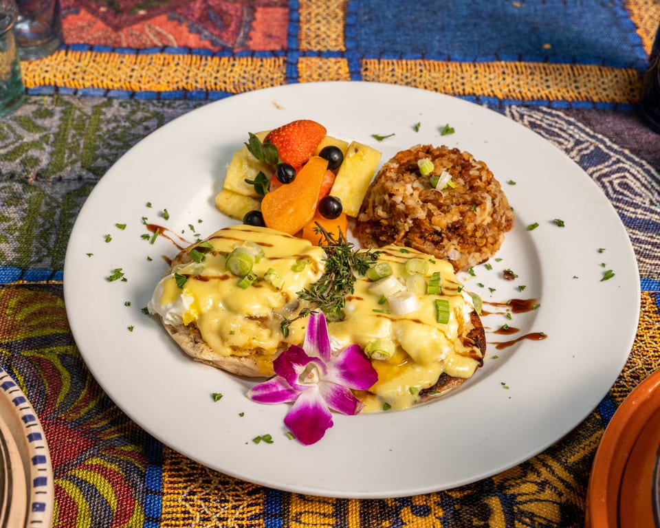 Eggs Benedict with hollandaise sauce, fruit salad, and hash browns on a white plate.
