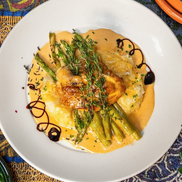 Roasted chicken with asparagus, mashed potatoes, and creamy sauce, garnished with fresh thyme.