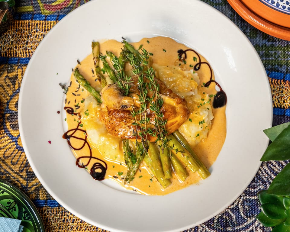 Roasted chicken with asparagus, mashed potatoes, and creamy sauce, garnished with fresh thyme.