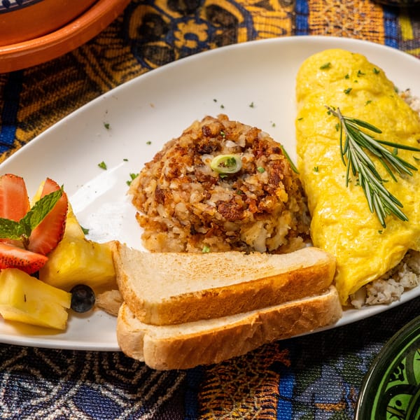 A breakfast plate with a yellow omelet, hash browns, toast, and a side of fresh fruit.