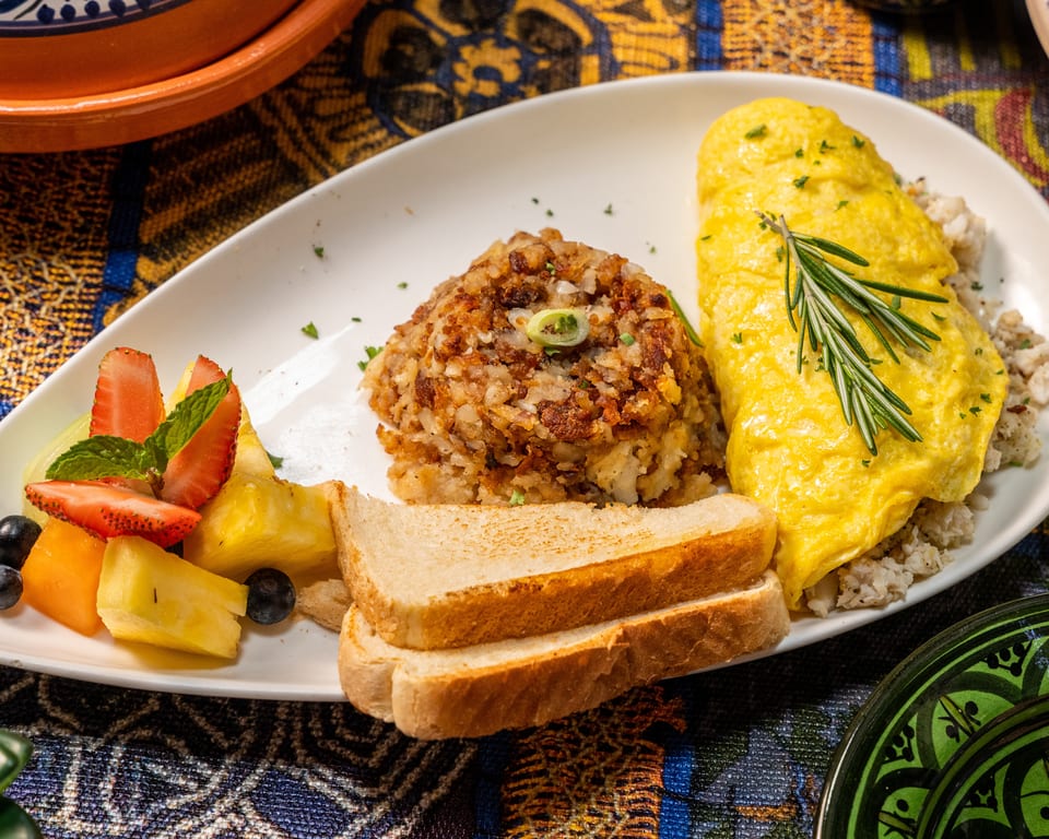 A breakfast plate with a yellow omelet, hash browns, toast, and a side of fresh fruit.