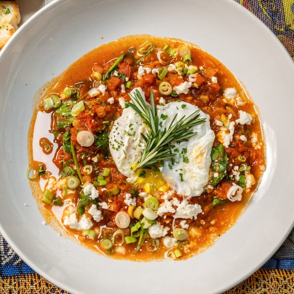 Shakshuka with poached eggs, feta, green onions, and rosemary, served with garlic bread.