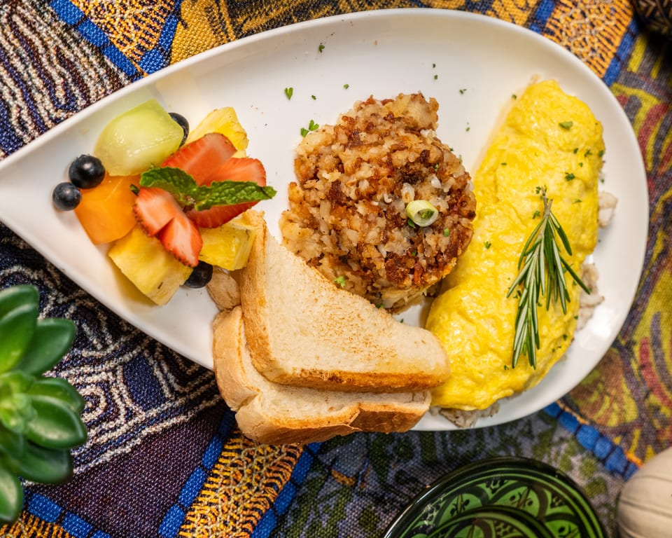 Breakfast plate with an omelet, hash browns, toast, and a fruit salad on a colorful tablecloth.