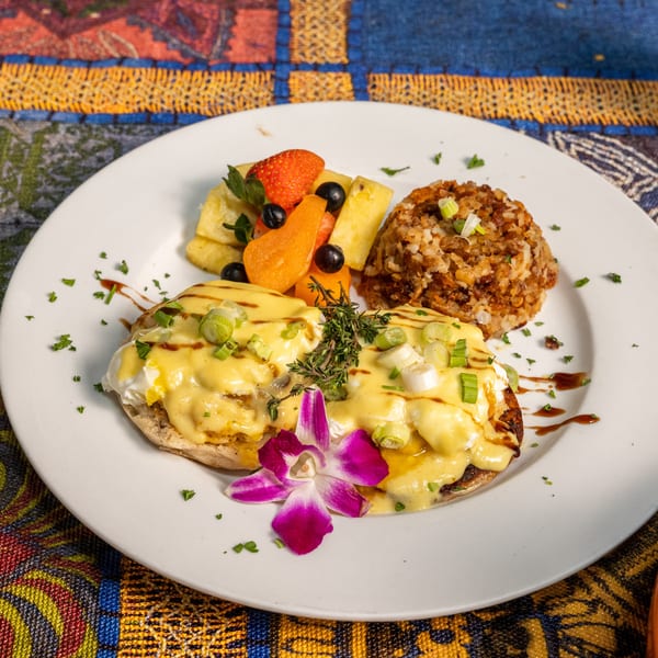 Eggs Benedict with hollandaise sauce, fruit salad, and hash browns on a colorful patterned tablecloth.