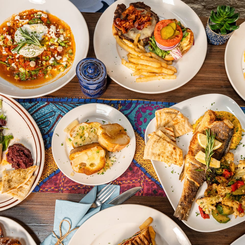 An overhead view of a table laden with various Mediterranean dishes, including seafood, burgers, and appetizers.