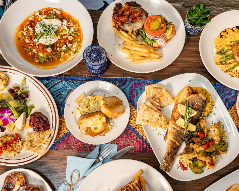 An overhead view of a table laden with various Mediterranean dishes, including seafood, burgers, and appetizers.
