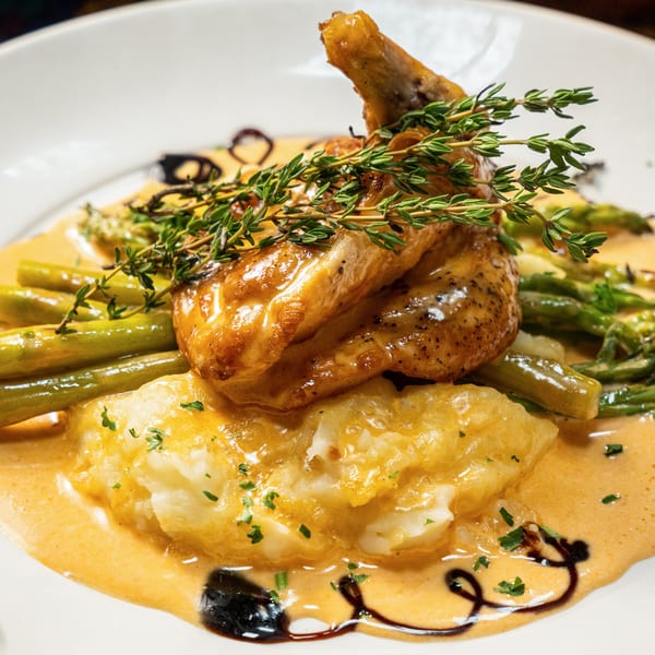 Roasted chicken with fresh thyme, asparagus, and mashed potatoes in a creamy sauce.