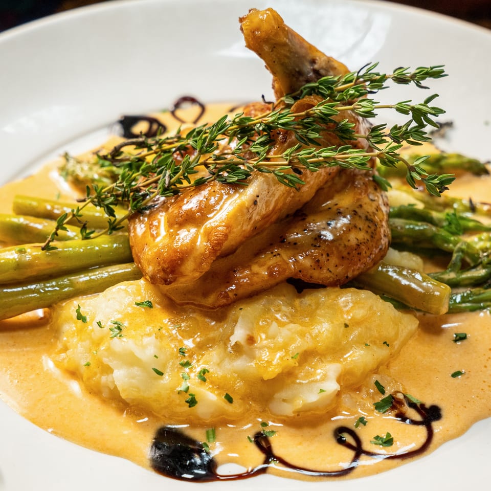 Roasted chicken with fresh thyme, asparagus, and mashed potatoes in a creamy sauce.