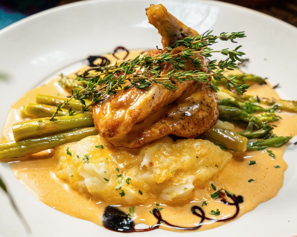 Roasted chicken with fresh thyme, asparagus, and mashed potatoes in a creamy sauce.