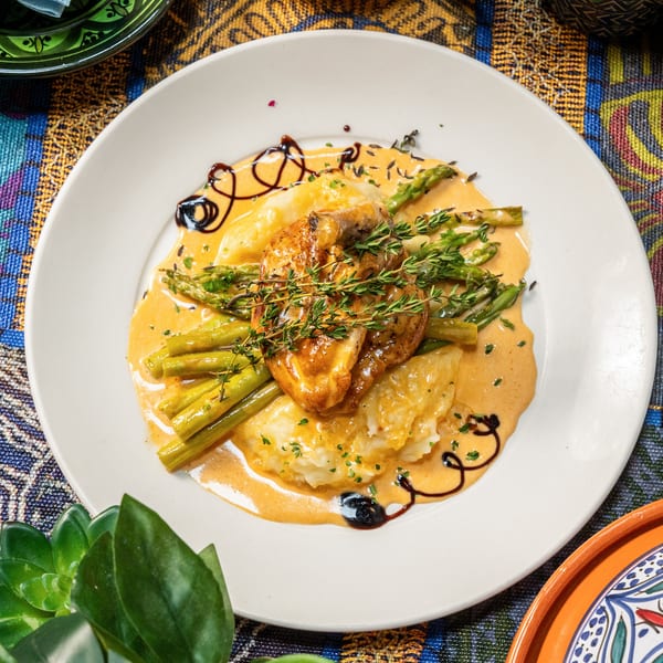 Chicken breast with mashed potatoes, asparagus, and creamy sauce on a white plate.