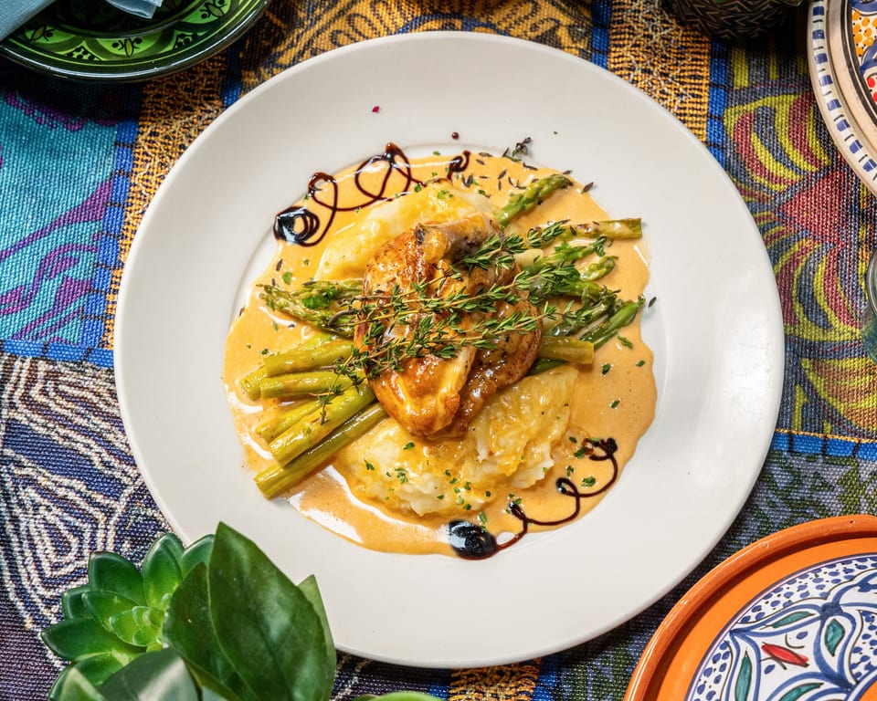 Chicken breast with mashed potatoes, asparagus, and creamy sauce on a white plate.