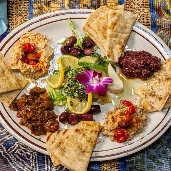 A colorful mezze platter with hummus, baba ghanoush, tabbouleh, olives, and pita bread.
