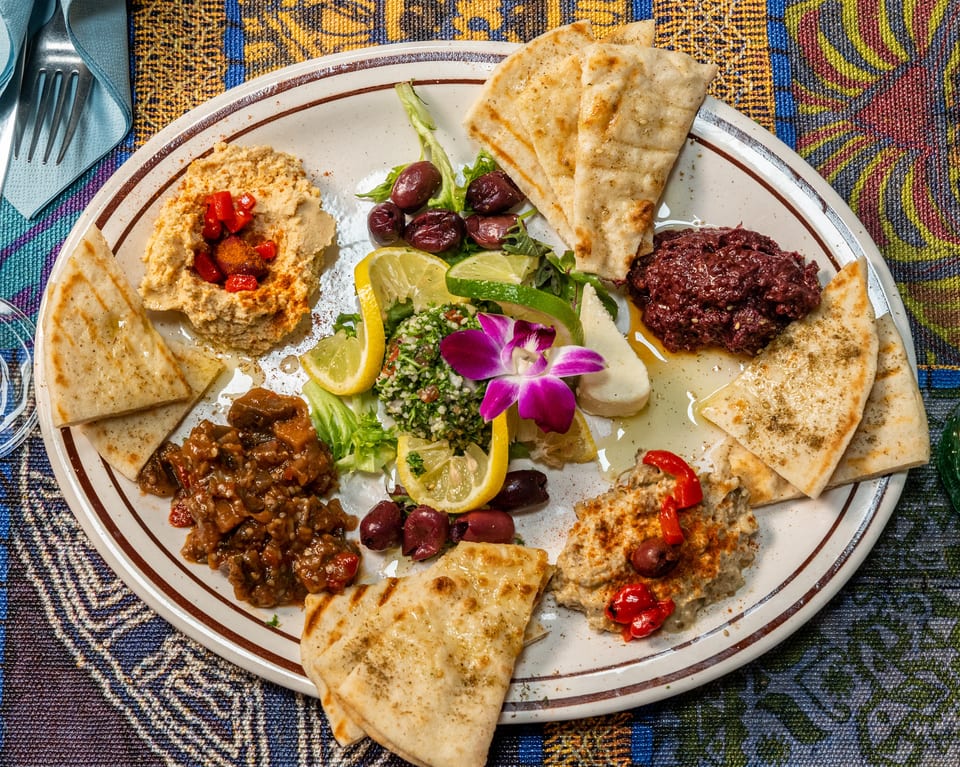 A colorful mezze platter with hummus, baba ghanoush, tabbouleh, olives, and pita bread.