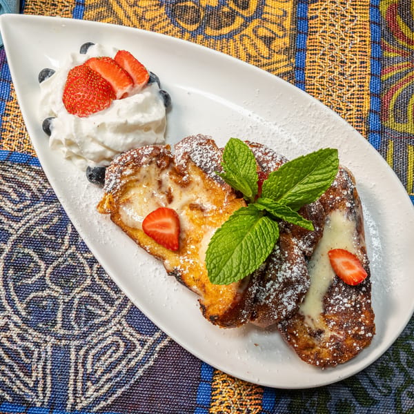 Golden French toast with cream, strawberries, blueberries, and mint on a white plate.