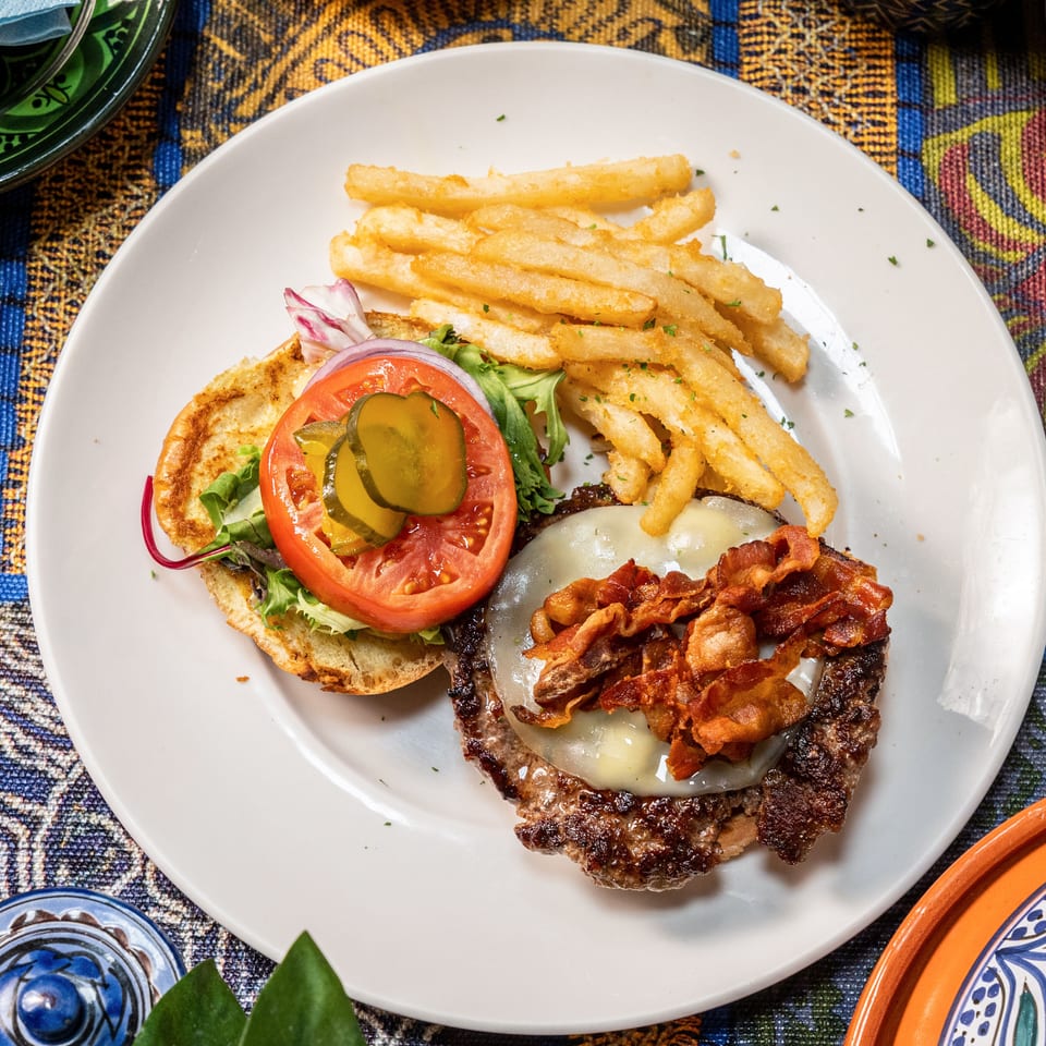 Overhead view of a bacon cheeseburger with fries, tomato, pickles, and onion on a white plate.